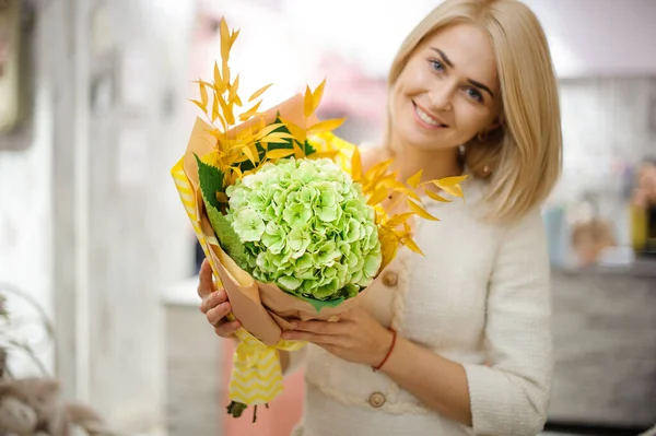 Gran ramo de hortensias y ramas amarillas en manos de una mujer sonriente — Foto de Stock