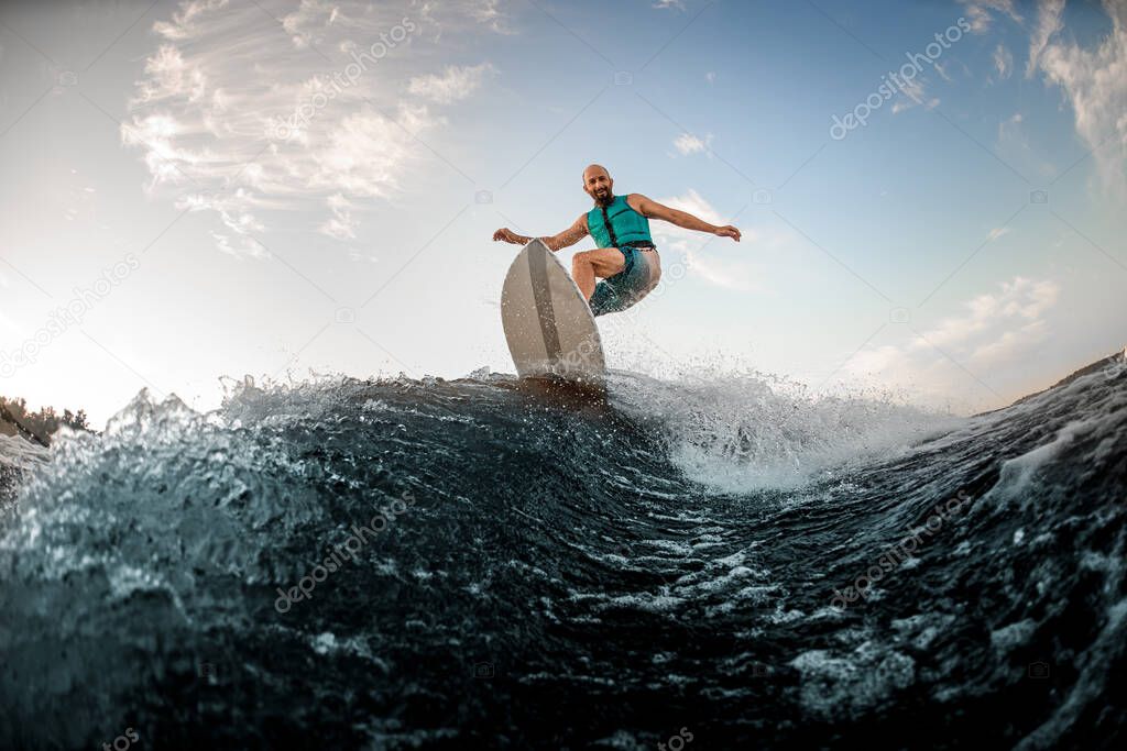 Active adult man wakesurfing on the board down the river