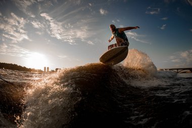 Wakesurfer aktif olarak gökyüzü ve günbatımında dalgaların üzerinden atlıyor.