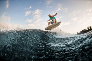 Enerjici adam nehir dalgalarının aşağısında, su tahtasına atlıyor. Wakesurf eğitimi
