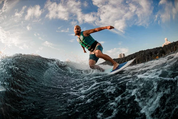 Homem atlético adulto em jaqueta de vida turquesa desce a onda em um wakesurf — Fotografia de Stock