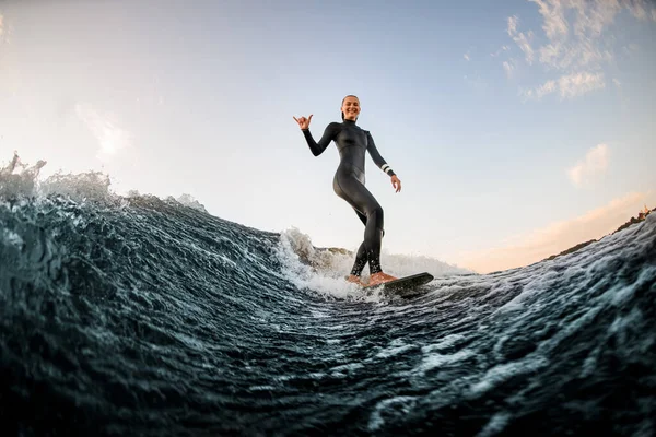 Žena v neoprénu wakesurfing na palubě a na koni po řece vlny a ukázat gesto ruky — Stock fotografie