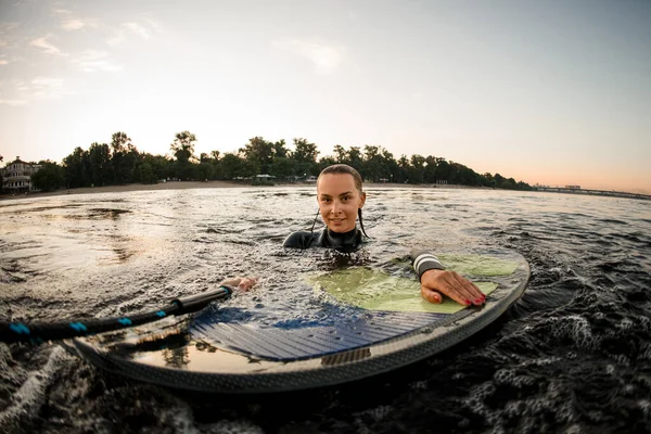 Vista della donna bagnata in muta in acqua appoggiata sul wakeboard — Foto Stock