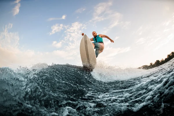 スポーティな男は波打ち際のウェイクボードに効果的にジャンプします。川でのウェイクサーフィン. — ストック写真
