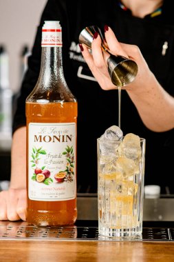 UKRAINE, KYIV - 11 Mart 2021: Barmen bardağa şerbet ve Monin 'den gelen tutku meyvesi şurubu ekleyerek kokteyl hazırlıyor