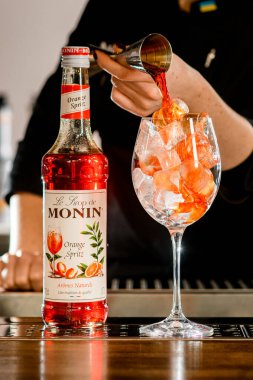 UKRAINE, KYIV - 11 Mart 2021: İçine barmenin sıvı döktüğü portakal suyu şurubu şişesi ve bir bardak buzun yakın çekimi