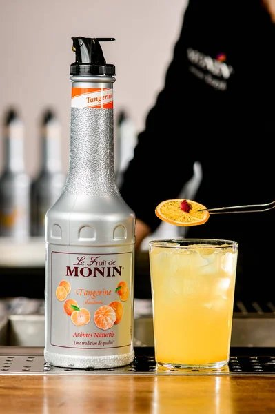 UKRAINE, KYIV - 11 maart 2021: barman siert glas met cocktail met fruit en fles mandarijnstroop van Monin staat vlakbij — Stockfoto
