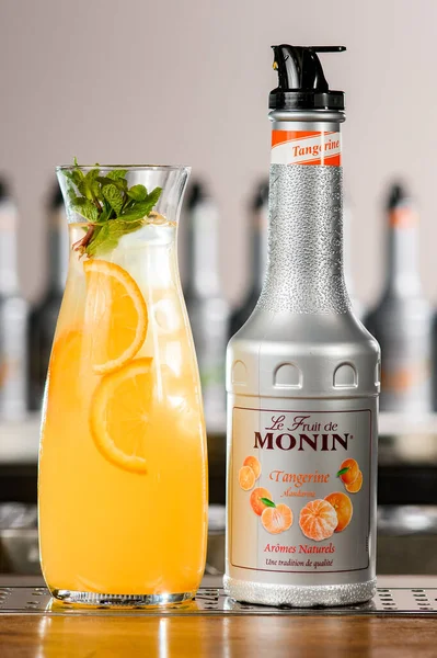 UKRAINE, KYIV - 11 maart 2021: Close-up van fles mandarijnensiroop van Monin en glazen karaf van ijscocktail met citrusschijfje — Stockfoto