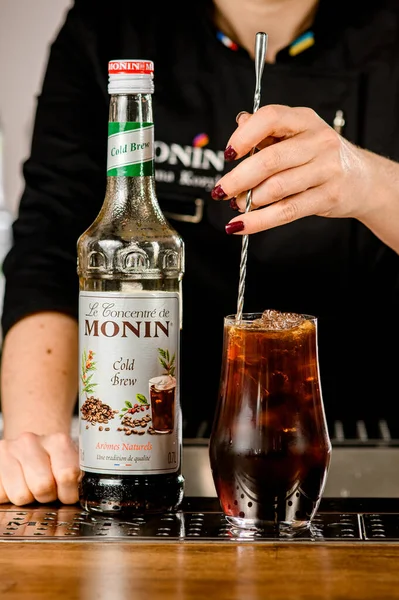 UKRAINE, KYIV - 11 maart 2021: barman roert cocktail in glas met lepel en fles koud brouwconcentraat van Monin staat in de buurt — Stockfoto