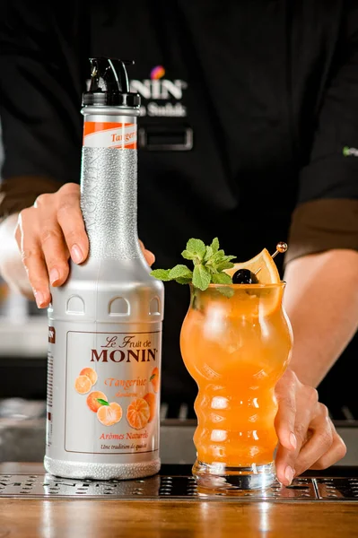 UKRAINE, KYIV - 11 maart 2021: vooraanzicht van fles mandarijnensiroop van Monin en glas cocktail met citrusschijfje en muntblad — Stockfoto