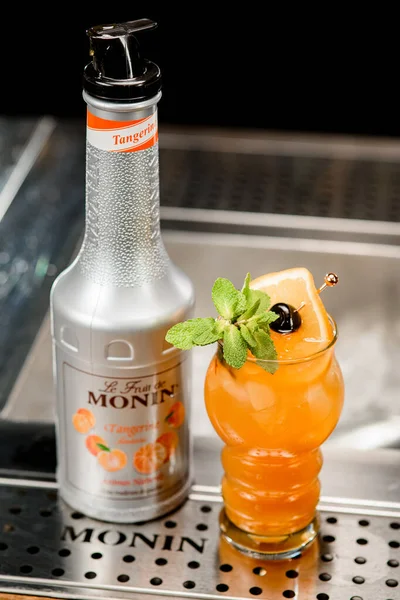 UKRAINE, KYIV - 11 maart 2021: bovenaanzicht van fles mandarijnstroop van Monin en glas cocktail met citrusschijfje en muntblad — Stockfoto