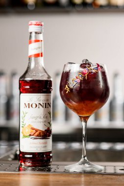 UKRAINE, KYIV - 11 Mart 2021: Monin 'in Sangria karışımı şurubu şişesinin önü ve güzel bir bardak soğuk kokteyl