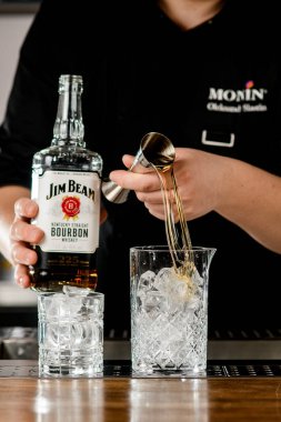 UKRAINE, KYIV - 11 Mart 2021: barmen viski şişesini tutuyor ve jigger kullanarak kristal karıştırma bardağına döküyor.