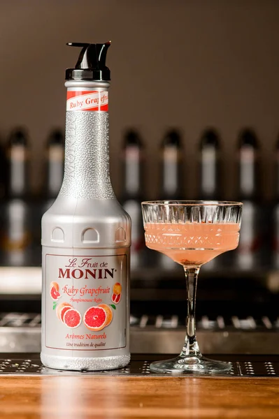 UKRAINE, KYIV - 11 MAART 2021: fles robijnpompelmoessiroop van Monin en kristalglas cocktail op bar — Stockfoto