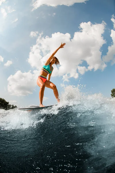 Активна жінка в барвистому купальнику енергійно балансує на хвилі на дошці . — стокове фото