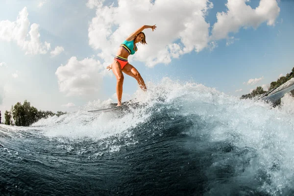 Mujer joven flexible en traje de baño colorido que se divierte y equilibra en la ola en la tabla de wakesurf. —  Fotos de Stock