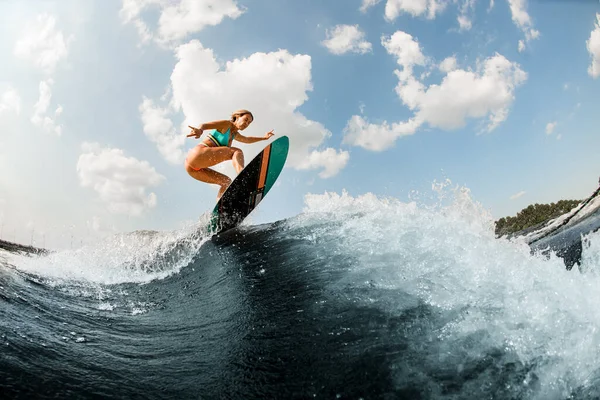 Despertador fêmea ativa habilmente pulando com wakeboard em espirrar onda do rio — Fotografia de Stock