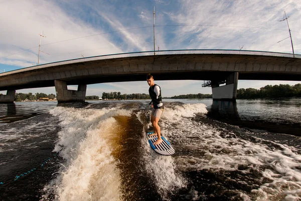 Armlös man rider våg på wakeboard mot bakgrund av bron — Stockfoto