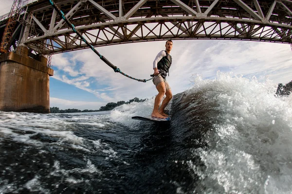 Homme en gilet de sauvetage tient la corde et monte vague sur planche de wakeboard — Photo