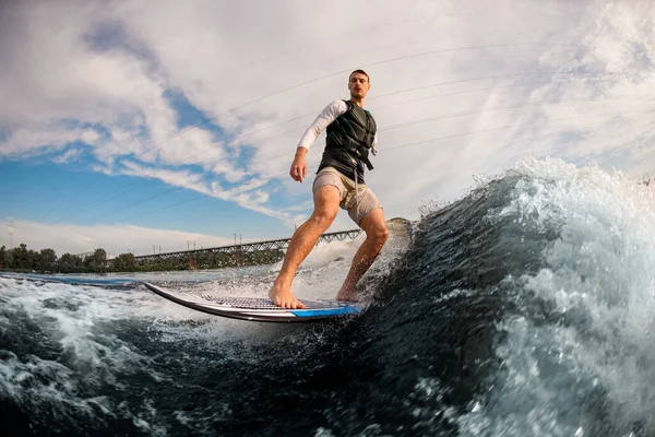 Jednoręki mężczyzna zbalansowany na wakeboardzie przez fale motorówki. Wakesurfing — Zdjęcie stockowe