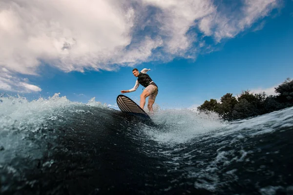 athletic one-armed man standing on surfboard and rides the wave. Wakesurfing on the river