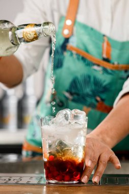 UKRAINE, KYIV - 12 Mart 2021: Barmenin şişeden sıvı döktüğü kızılcıklı lezzetli soğuk kokteyllerin önü