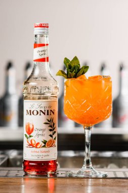 UKRAINE, KYIV - 12 Mart 2021: Bir şişe Monin portakal şurubu ve tezgahın üzerinde parlak turuncu kokteyl önü