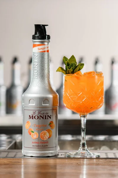 UKRAINE, KYIV - 12 maart 2021: Fles Monin Tangerine siroop en een glas heldere oranje cocktail op de bar — Stockfoto