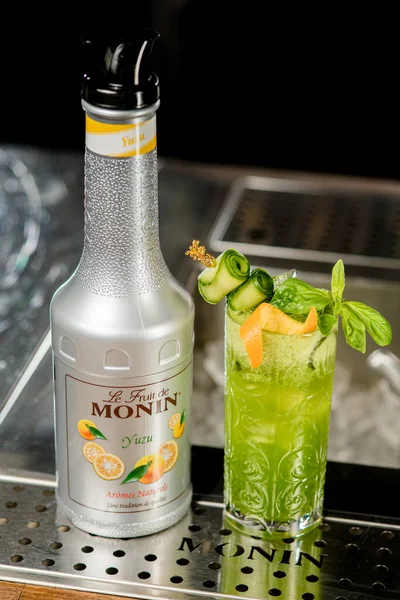 UKRAINE, KYIV - Maart 12, 2021: hoek uitzicht op fles Monin yuzu puree en glas koude groene cocktail op bar teller — Stockfoto