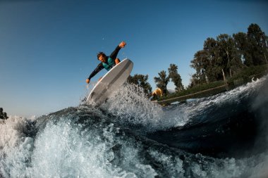 Wakesurfer mavi gökyüzünün arka planında sıçrayan motorlu tekne dalgasına atlıyor.