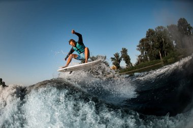 wakesurfer mavi gökyüzünün arka planında motorlu teknenin yüksek dalgasına atlıyor