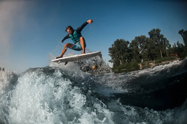 Adulto energia wakesurfer pulando a bordo sobre ondas contra o céu azul e árvores verdes — Fotografia de Stock