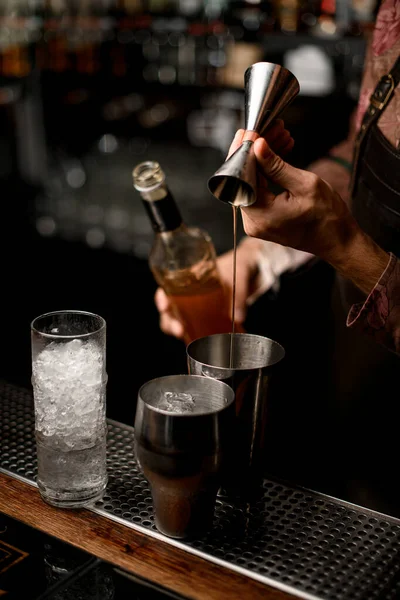 Hand of barman masterfully pours drink from jigger into steel shaker glass — Stock Photo, Image