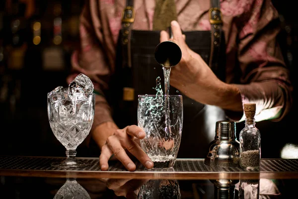 Genomskinliga glas i ett av vilka handen av man bartender häller dryck från jigger — Stockfoto