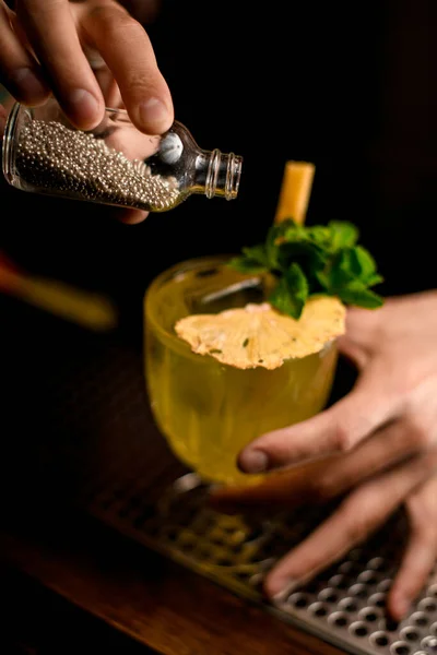 Pequeña botella con pequeñas bolas plateadas utilizadas para decorar alimentos y bebidas en la mano del hombre — Foto de Stock