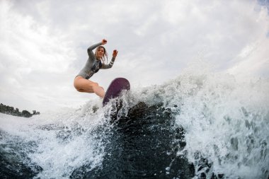 Gri dalgıç kıyafetli güzel, esnek bir kadın. Nehir dalgası üzerinde dengede duruyor.