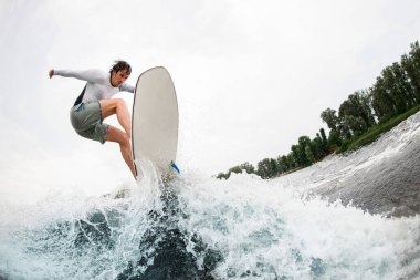 Enerjik bir adam eğleniyor ve yaz günü sörf tahtasında dalgalara atlıyor..