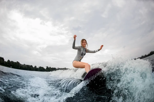 Aktive Frau steht auf Wakeboard und reitet auf Welle gegen bewölkten Himmel — Stockfoto