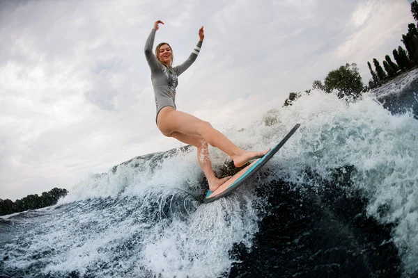 Ottima vista di donna attraente sul wakeboard cavalca giù sull'onda contro un cielo nuvoloso — Foto Stock