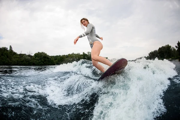 柔軟な女性でグレー水着巧みに上の波に乗って上のウェイクサーフボード. — ストック写真