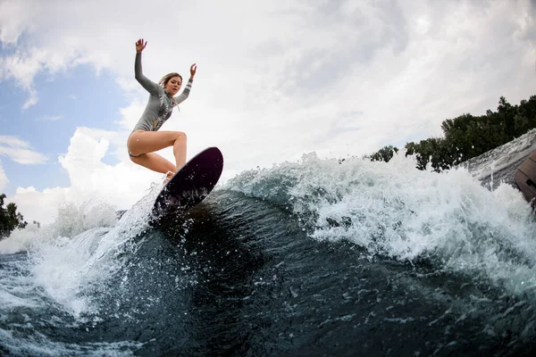 Belle femme active en combinaison grise sur wakesurf promenades sur une grande vague éclaboussante — Photo