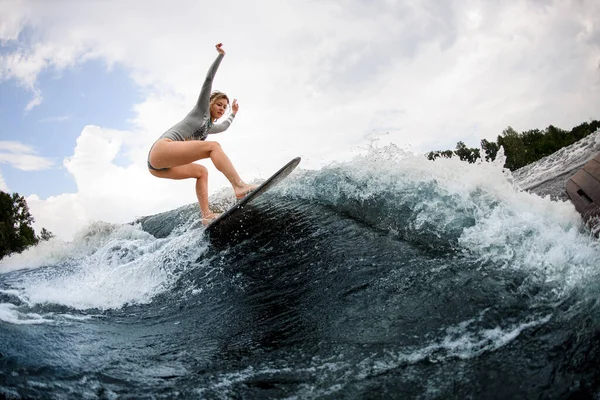 Atlético e flexível mulher habilmente montando na onda na placa wakesurf. — Fotografia de Stock