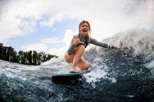 Femme s'amuser et descend la vague assis sur un wakeboard et montrer geste de la main. — Photo
