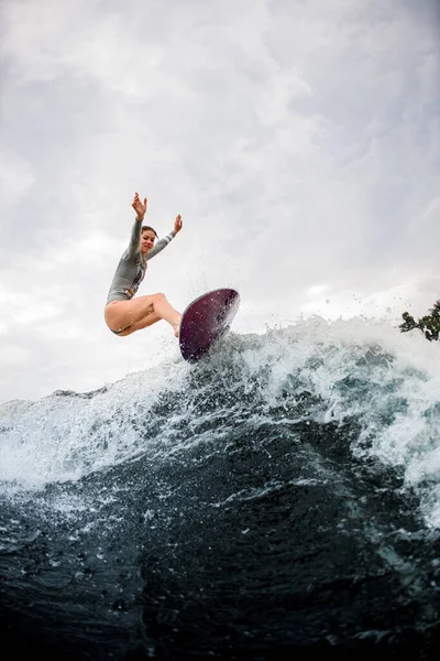Mujer enérgica cabalga por la ola en tabla de wakesurf. Cielo nublado sobre fondo —  Fotos de Stock