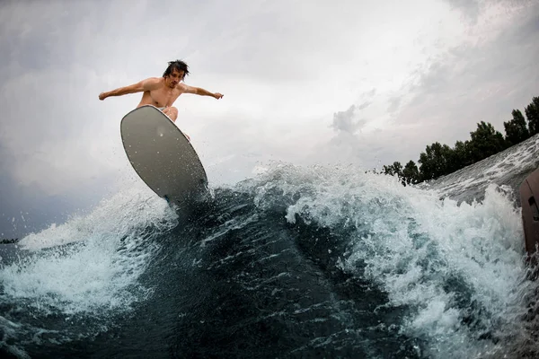 Grande visão do homem de energia forte habilmente pulando sobre onda salpicando na placa wakesurf. — Fotografia de Stock