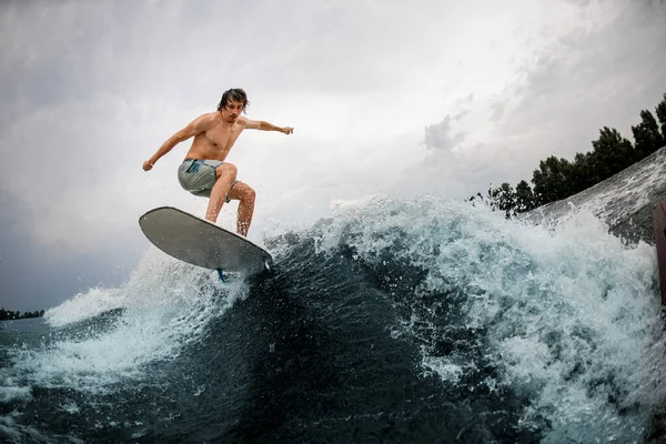 Grande vista do homem de energia forte habilmente pulando sobre a onda do rio espirrando na placa de wakesurf. — Fotografia de Stock