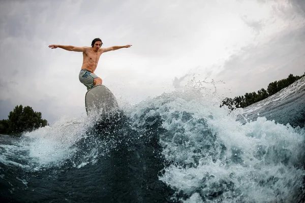 Vista maravilhosa sobre a onda salpicando e homem esportivo habilmente pulando sobre ele — Fotografia de Stock