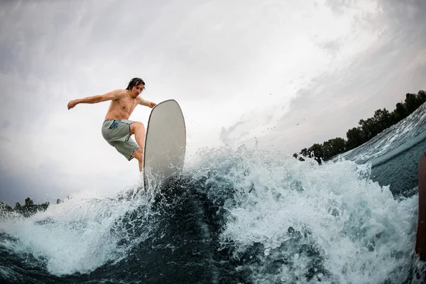 Hombre deportivo hábilmente cabalga hasta salpicar ola en tabla wakesurf. — Foto de Stock