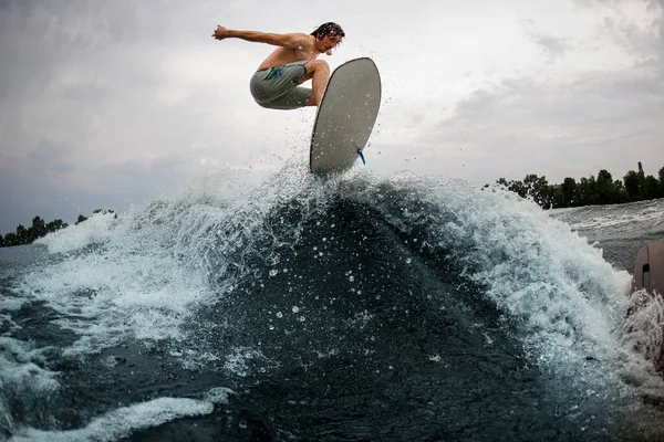 Uomo sportivo salta abilmente sopra onda schizzi sul bordo wakesurf. — Foto Stock