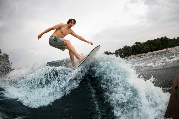 Energia esportiva homem habilmente cavalga até a onda salpicando em wakesurf bordo. — Fotografia de Stock